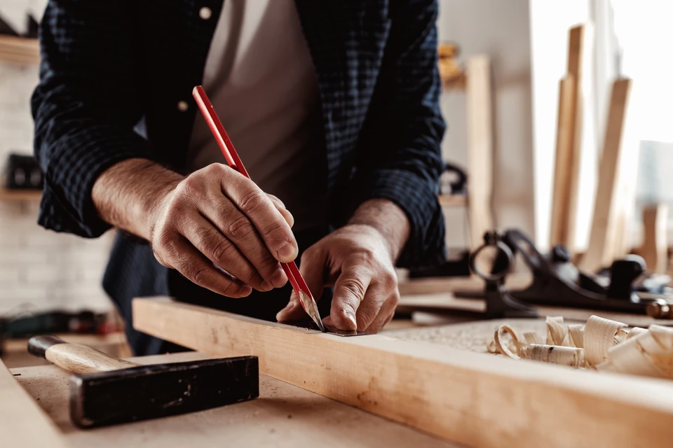 Artisan menuisier travaillant dans son atelier, marquant pr&eacute;cis&eacute;ment une planche de bois avec un crayon rouge