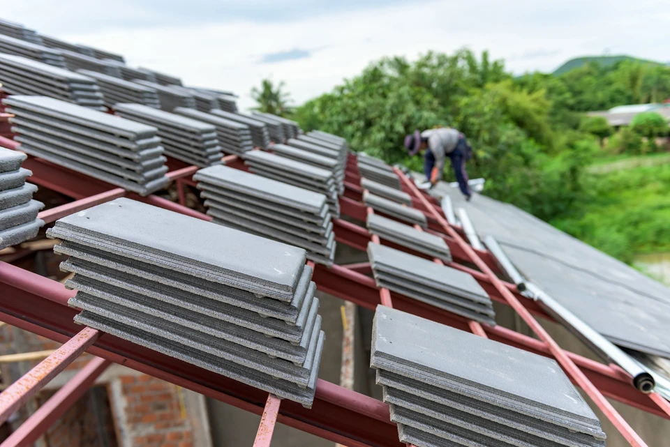Chantier de toiture en cours avec ouvrier installant des tuiles plates grises sur charpente &agrave; structure m&eacute;tallique rouge
