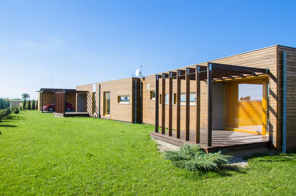 Maison contemporaine modulaire en bois avec terrasse couverte et pergola à lames verticales sur terrain verdoyant