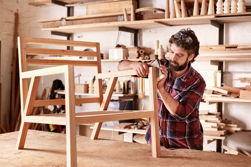 Artisan menuisier barbu en chemise à carreaux travaille dans son atelier, assemblant une chaise en bois massif