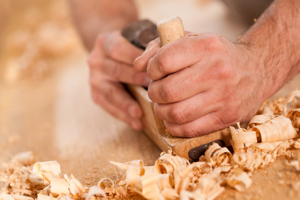 Artisan travaillant le bois avec un rabot à main, produisant des copeaux fins sur établi
