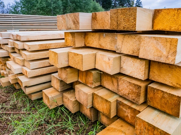 Ouvrier en combinaison grise effectue des mesures dans une structure en bois en construction, utilisant un mètre ruban jaune